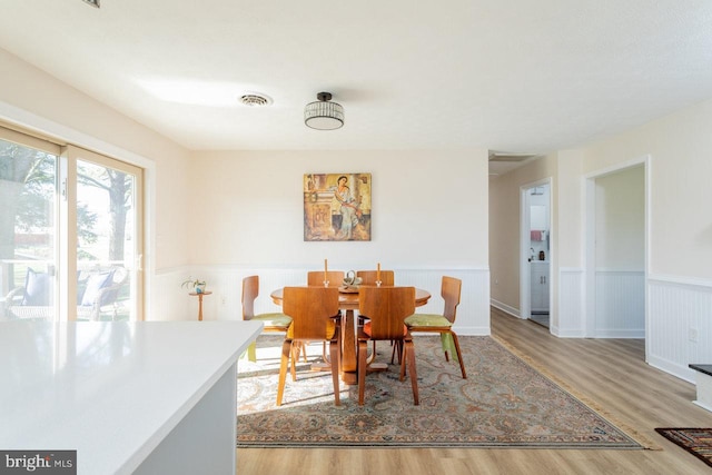 dining area with wood finished floors, visible vents, and a wainscoted wall