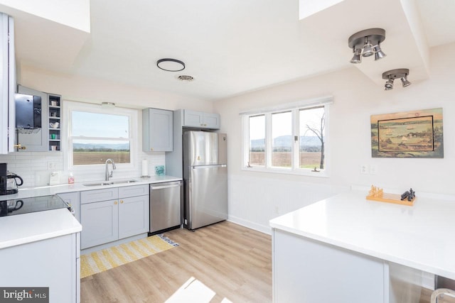 kitchen with a sink, light countertops, appliances with stainless steel finishes, light wood-style flooring, and decorative backsplash