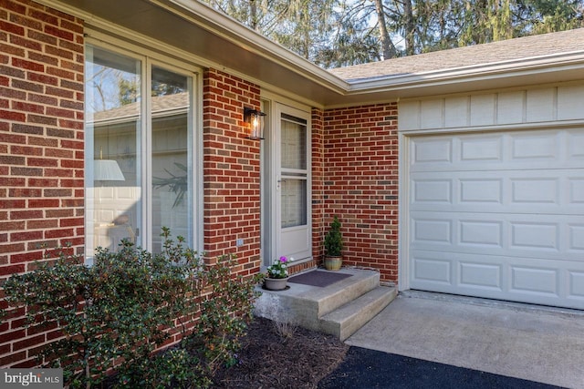 entrance to property featuring a garage, brick siding, and driveway