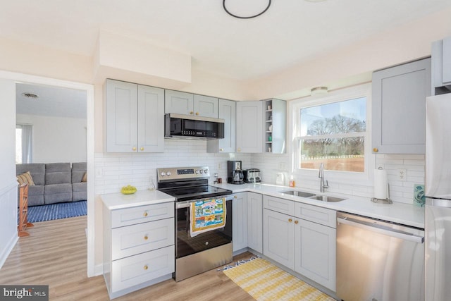kitchen featuring light wood-type flooring, gray cabinets, a sink, stainless steel appliances, and backsplash
