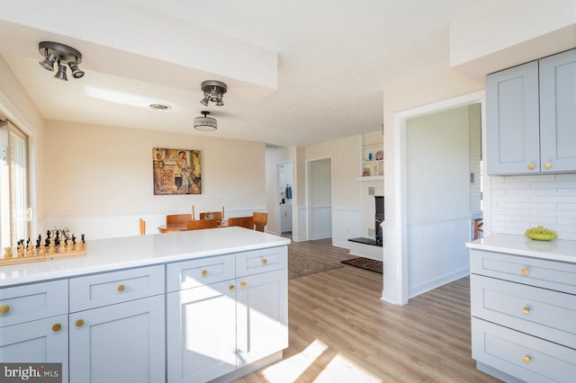 kitchen with visible vents, a fireplace with raised hearth, light countertops, a peninsula, and light wood finished floors