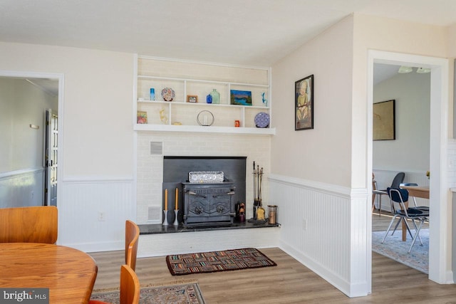 living area with visible vents, a fireplace, crown molding, wood finished floors, and a wainscoted wall