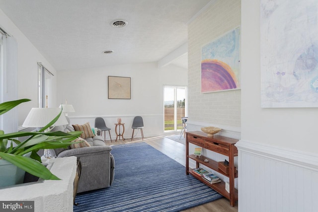 living area featuring wainscoting, visible vents, vaulted ceiling with beams, and wood finished floors
