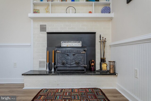 interior details featuring a fireplace, visible vents, a wainscoted wall, and wood finished floors