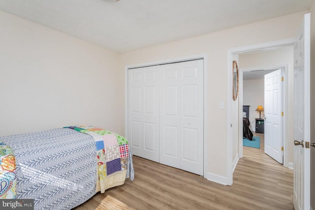 bedroom with a closet, light wood-style flooring, and baseboards
