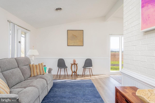 living area with wood finished floors, lofted ceiling with beams, visible vents, and plenty of natural light