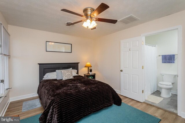 bedroom with connected bathroom, a ceiling fan, visible vents, wood finished floors, and baseboards