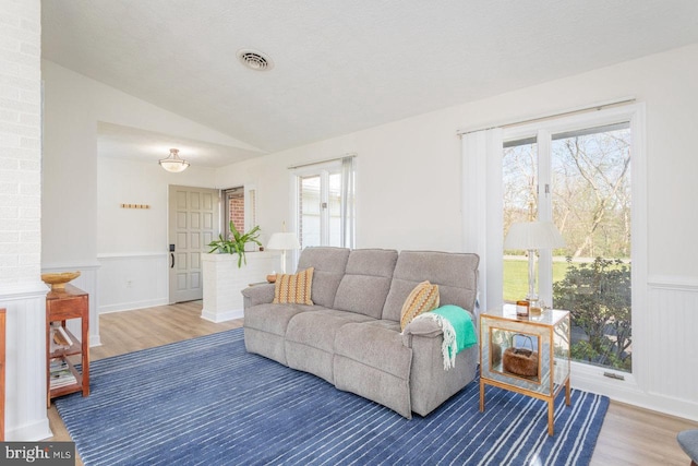 living area with wainscoting, lofted ceiling, visible vents, and wood finished floors