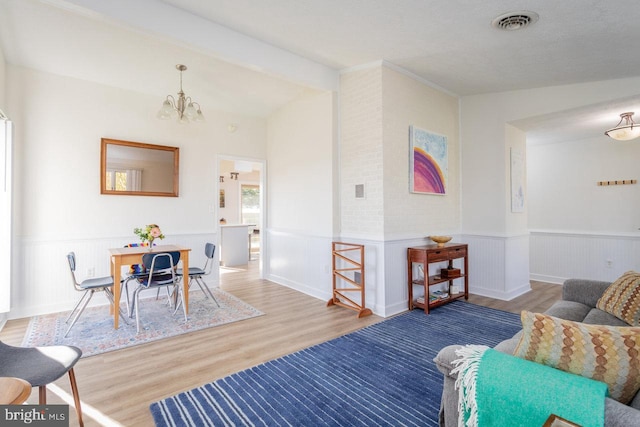 living area with a notable chandelier, wainscoting, visible vents, lofted ceiling, and wood finished floors