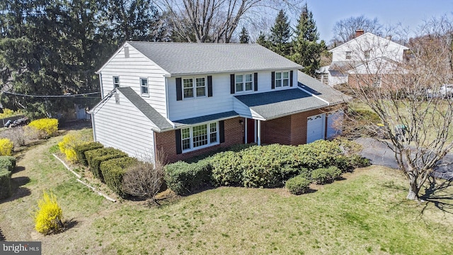 traditional-style house featuring a front yard, brick siding, an attached garage, and a shingled roof