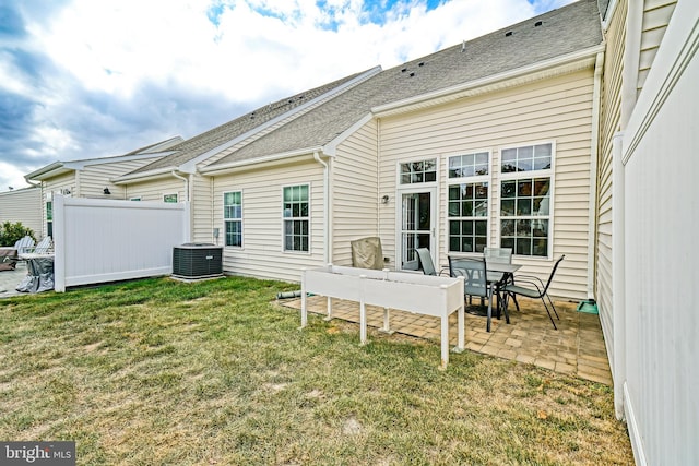 rear view of house with a patio, roof with shingles, central AC unit, fence, and a lawn