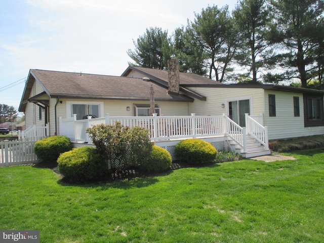 rear view of property featuring a lawn, a chimney, roof with shingles, and a deck