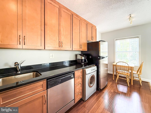 kitchen with stainless steel dishwasher, dark countertops, a sink, washer / clothes dryer, and dark wood-style floors