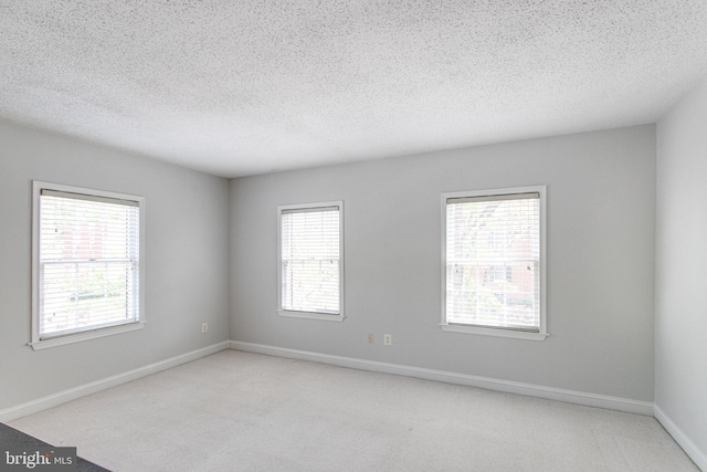 empty room featuring light carpet, a textured ceiling, and baseboards