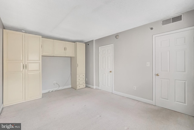 unfurnished bedroom featuring a textured ceiling, baseboards, visible vents, and light colored carpet