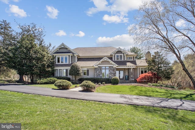 craftsman house featuring a front lawn, stone siding, and a chimney