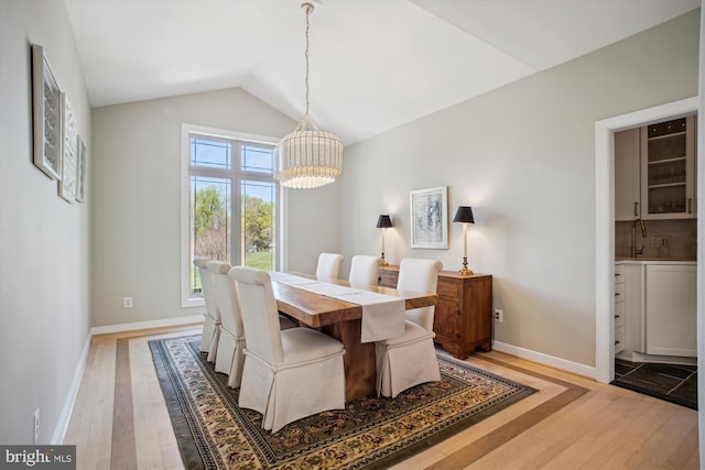dining room with light wood-type flooring, vaulted ceiling, baseboards, and a notable chandelier