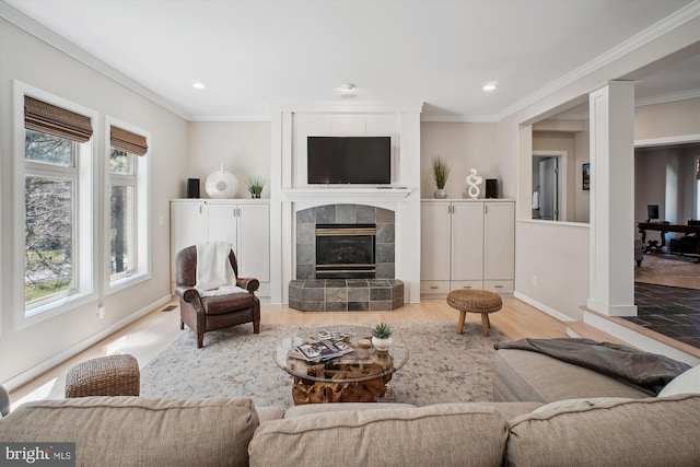 living area featuring a tiled fireplace, crown molding, wood finished floors, and plenty of natural light