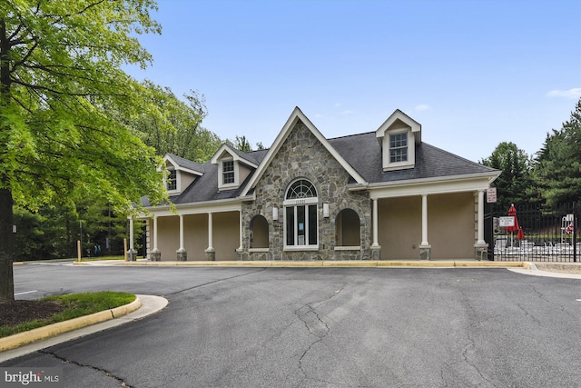 new england style home with stucco siding, stone siding, and fence
