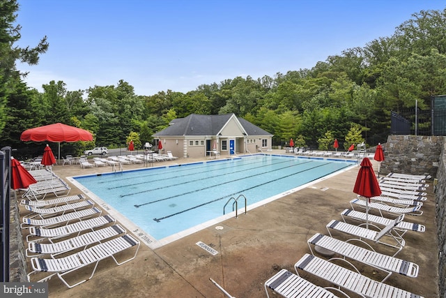 pool with a patio area, fence, and a forest view