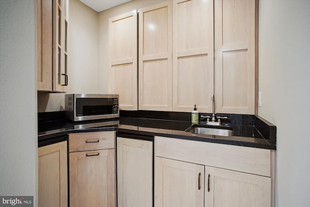 kitchen with stainless steel microwave, dark countertops, light brown cabinetry, and a sink