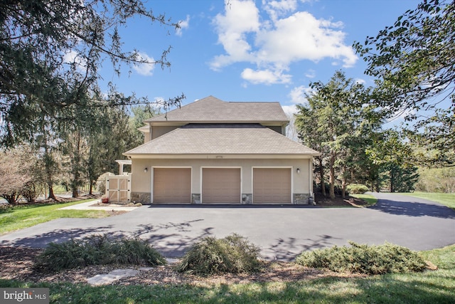 view of side of home with an attached garage, aphalt driveway, stucco siding, and stone siding