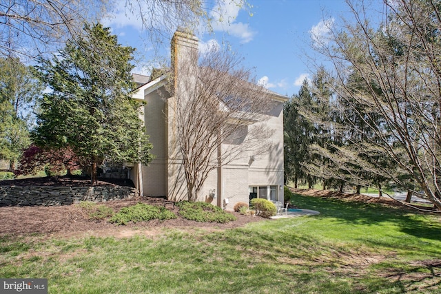 view of side of home with brick siding, a yard, and a chimney