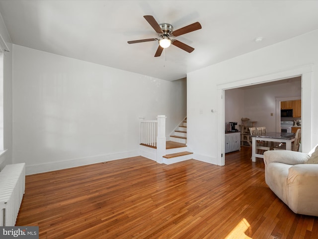 living room featuring radiator, baseboards, a ceiling fan, stairway, and wood-type flooring
