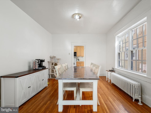 dining space with radiator heating unit, baseboards, and wood finished floors