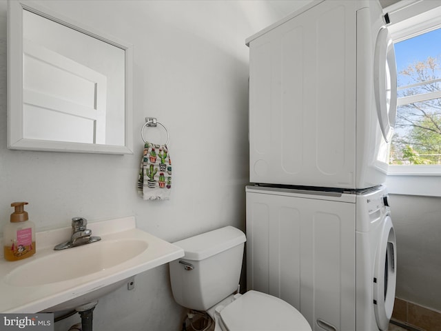 half bathroom with a wealth of natural light, toilet, stacked washer / dryer, and a sink