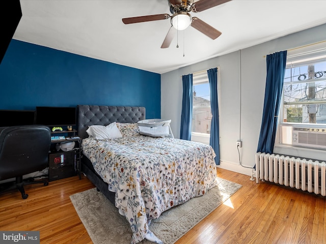 bedroom with multiple windows, cooling unit, wood finished floors, and radiator