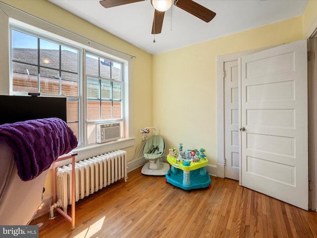 bedroom with a ceiling fan, radiator heating unit, wood finished floors, cooling unit, and baseboards