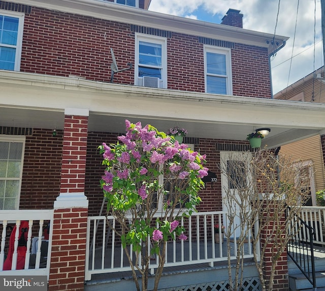doorway to property with covered porch, a chimney, and brick siding