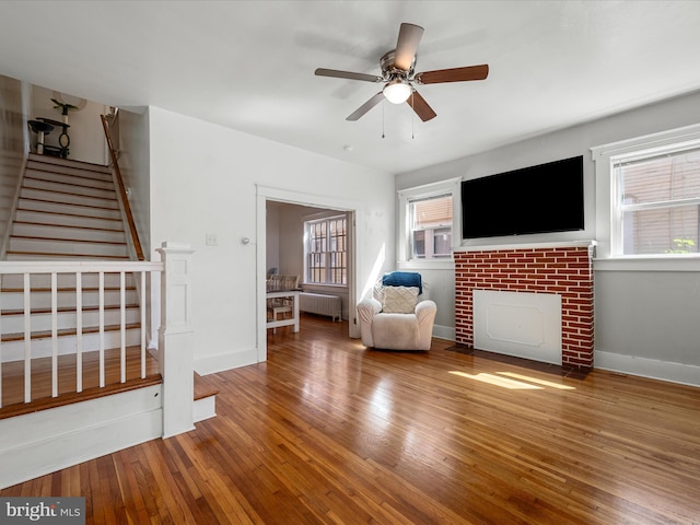 living area featuring radiator, a fireplace with flush hearth, stairway, wood-type flooring, and ceiling fan