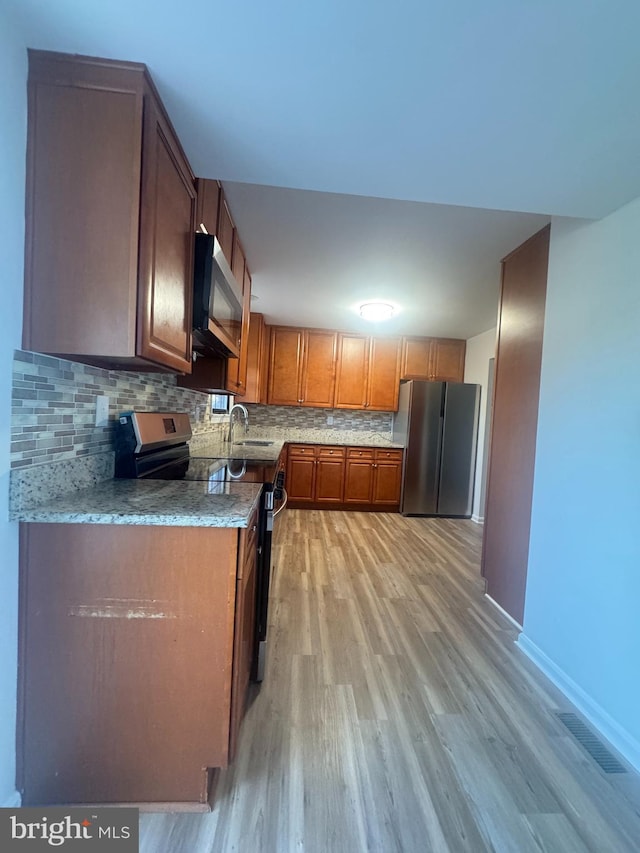 kitchen featuring visible vents, appliances with stainless steel finishes, brown cabinets, light wood finished floors, and backsplash