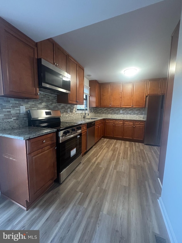 kitchen with light wood-type flooring, appliances with stainless steel finishes, a sink, and backsplash