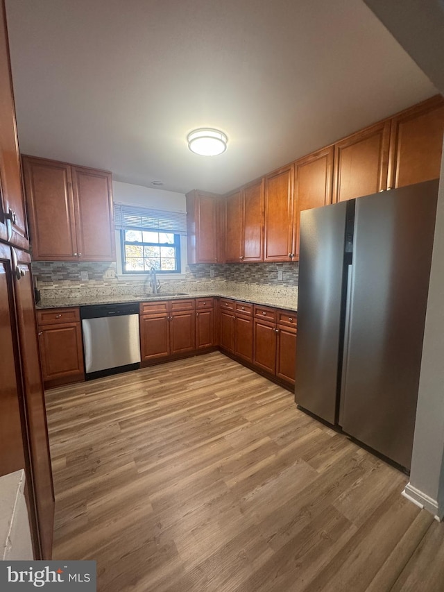 kitchen featuring stainless steel appliances, light wood-style floors, brown cabinetry, and decorative backsplash