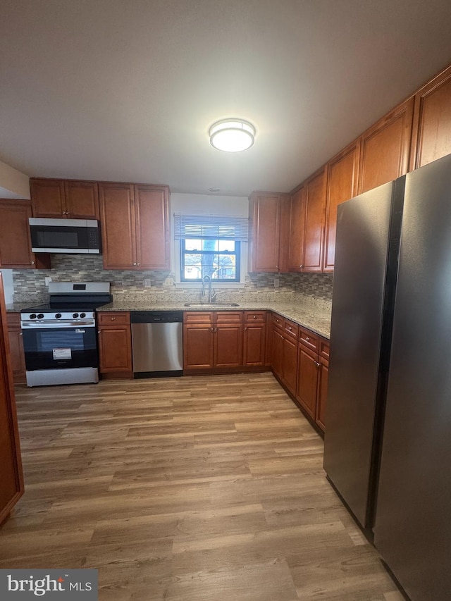 kitchen featuring tasteful backsplash, light wood-type flooring, brown cabinets, appliances with stainless steel finishes, and a sink