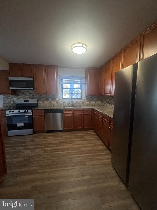 kitchen featuring dark wood finished floors, a sink, stainless steel appliances, brown cabinets, and backsplash