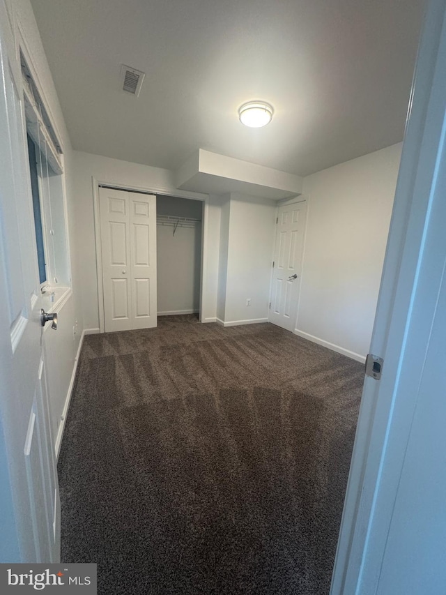 unfurnished bedroom with baseboards, a closet, dark colored carpet, and visible vents