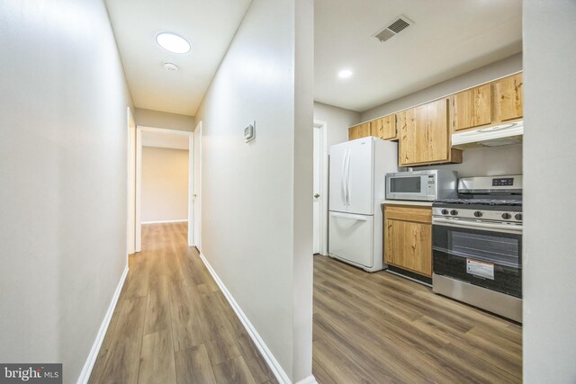 kitchen featuring visible vents, wood finished floors, baseboards, under cabinet range hood, and white appliances