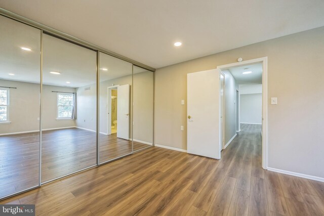 unfurnished bedroom with baseboards, recessed lighting, wood finished floors, and a closet