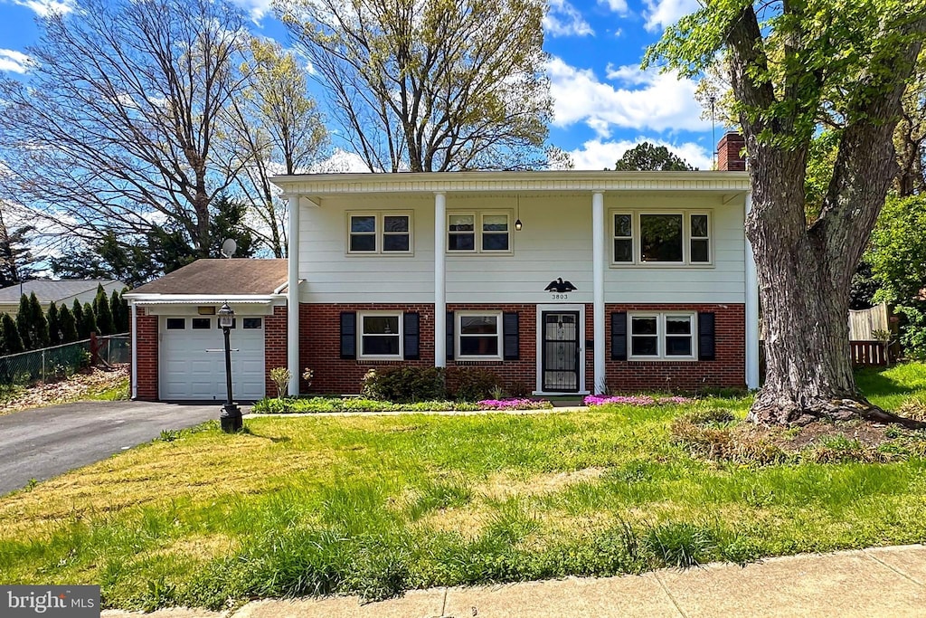 greek revival house featuring brick siding, an attached garage, aphalt driveway, and fence