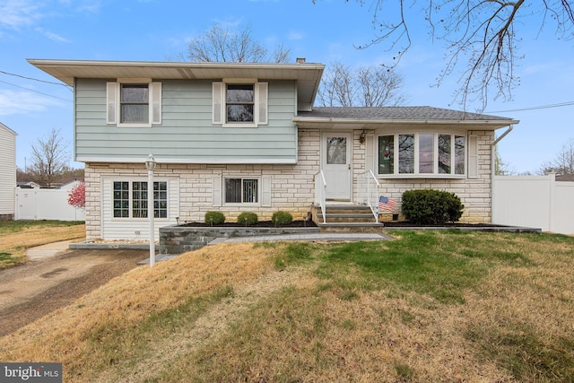 tri-level home featuring a shingled roof, a chimney, fence, and a front lawn
