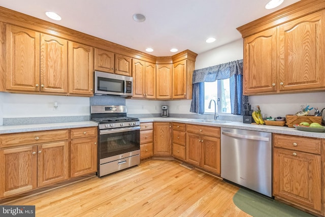 kitchen featuring light wood-style flooring, light countertops, a sink, stainless steel appliances, and brown cabinets