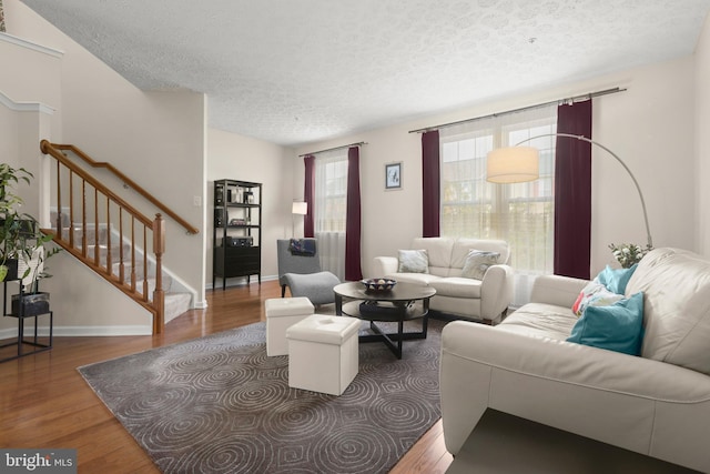living room featuring a textured ceiling, stairway, wood finished floors, and baseboards