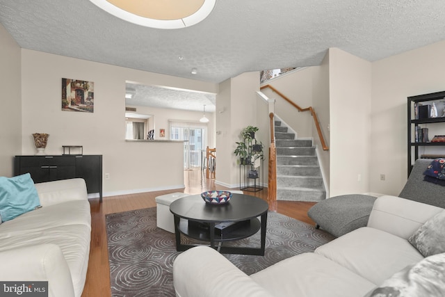 living area with stairway, a textured ceiling, baseboards, and wood finished floors