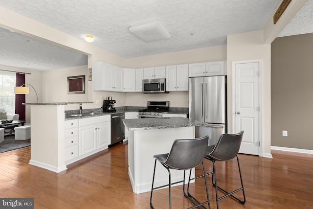 kitchen with a kitchen bar, a sink, white cabinets, a textured ceiling, and appliances with stainless steel finishes