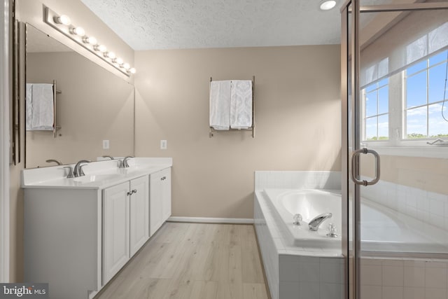 full bathroom with double vanity, wood finished floors, a sink, a bath, and a textured ceiling