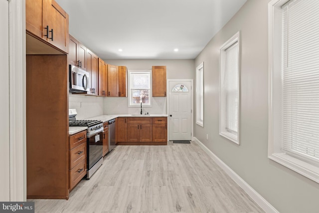 kitchen with brown cabinetry, light wood-style flooring, light countertops, a sink, and stainless steel appliances
